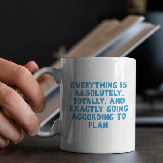 White mug with blue text held by a hand, placed on a surface with a blurred background