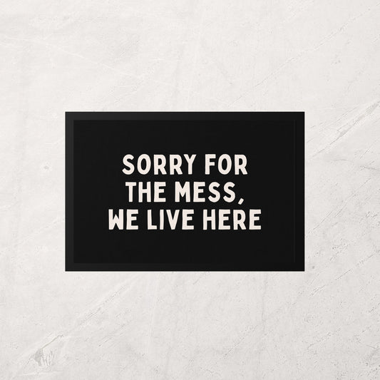 Doormat with text 'Sorry for the mess, we live here' on a textured white background