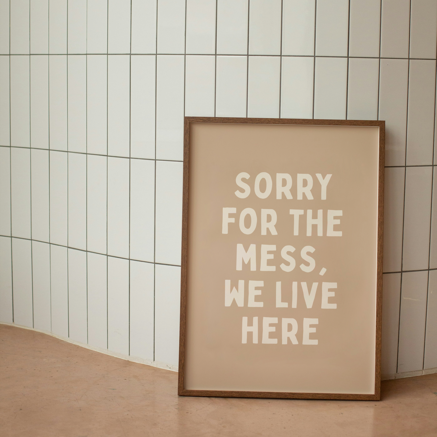 Framed poster with 'Sorry for the mess, we live here' text on a tiled wall.