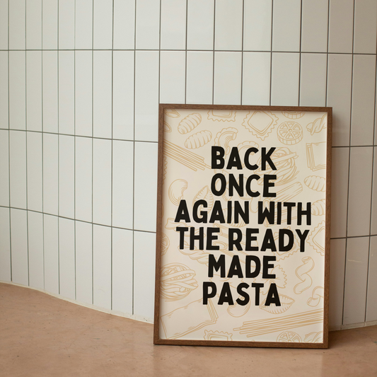 A framed art print with the text 'BACK ONCE AGAIN WITH THE READY MADE PASTA' written in black on a cream background, displayed against a wall with white tiles.