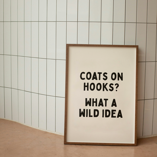 Framed poster with text 'Coats on hooks? What a wild idea' against a tiled wall.