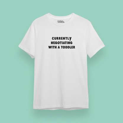 White t-shirt with text 'Currently Negotiating with a Toddler' on a light green background