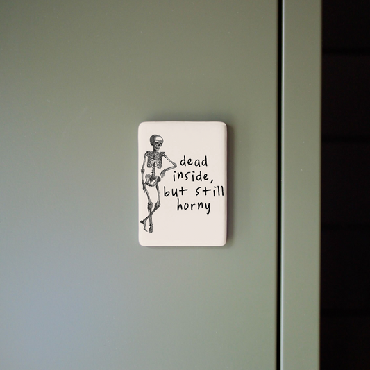Small rectangular sign with a skeleton illustration and text on a gray wall.