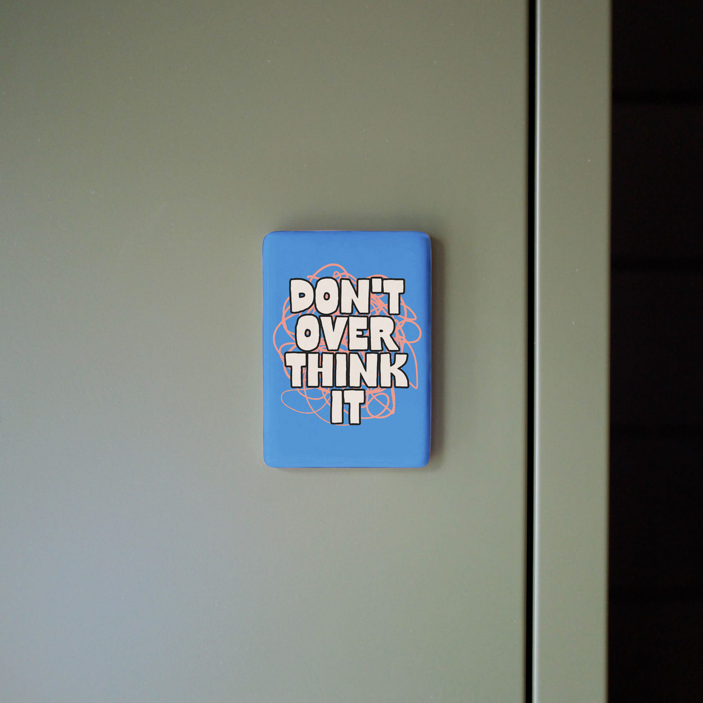 Blue magnet with 'DON'T OVER THINK IT' text on a refrigerator door