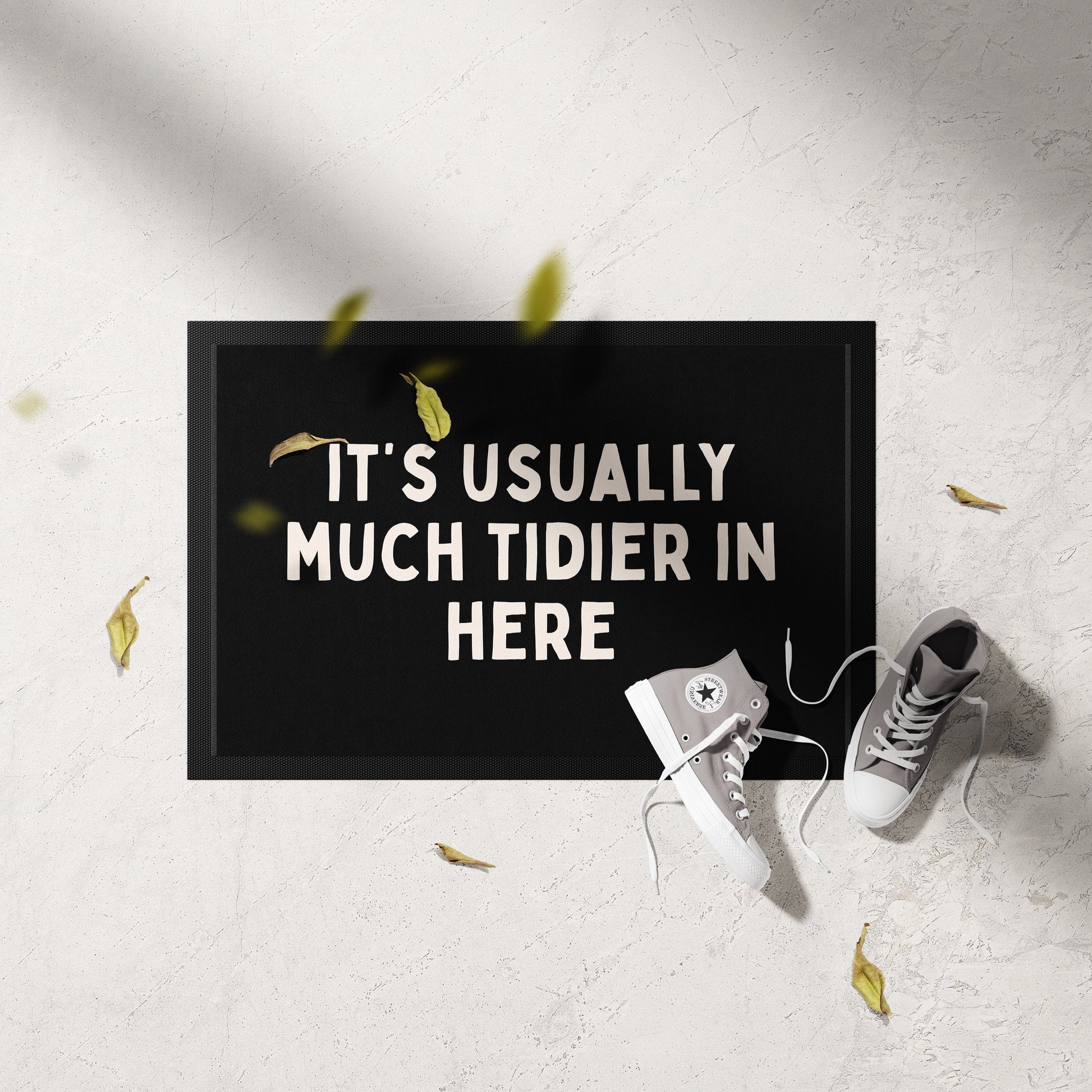 Doormat with humorous text on a light gray floor with shoes and leaves.