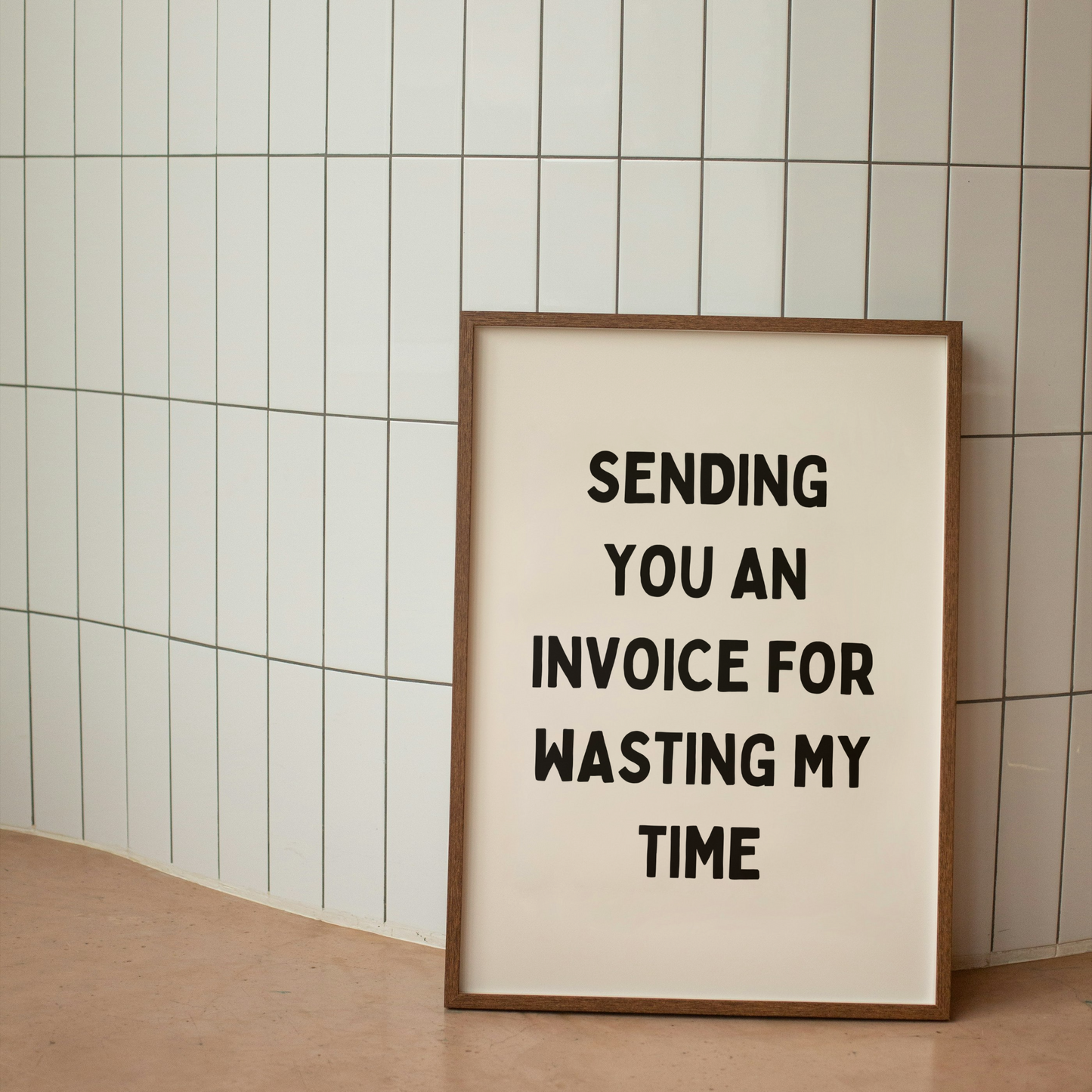 Framed poster with text 'Sending you an invoice for wasting my time' against a tiled wall.