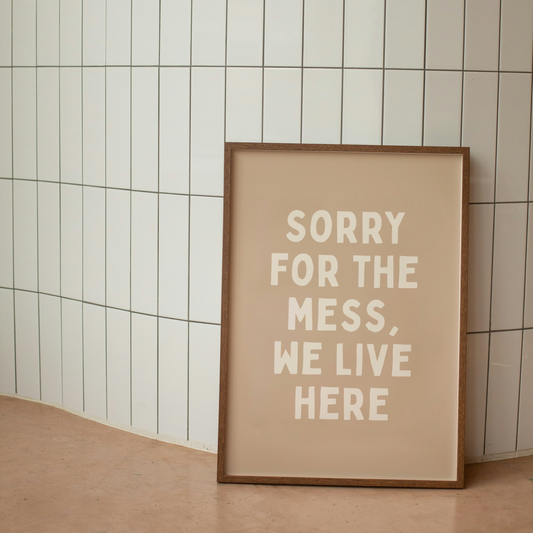 Framed poster with 'Sorry for the mess, we live here' text on a tiled wall.