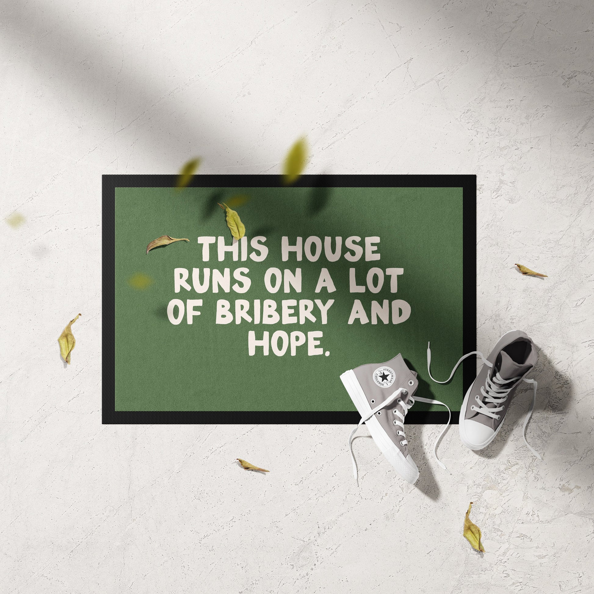 Doormat with text 'This house runs on a lot of bribery and hope' on a light gray floor.