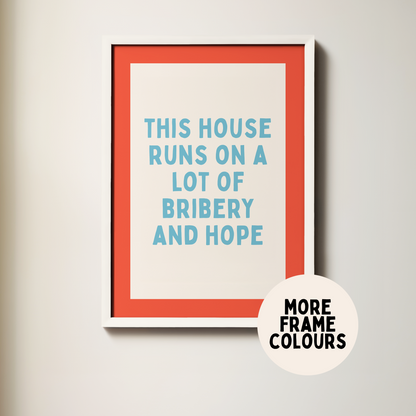 Framed poster with text 'This house runs on a lot of bribery and hope' on a plain wall.
