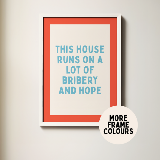 Framed poster with text 'This house runs on a lot of bribery and hope' on a plain wall.