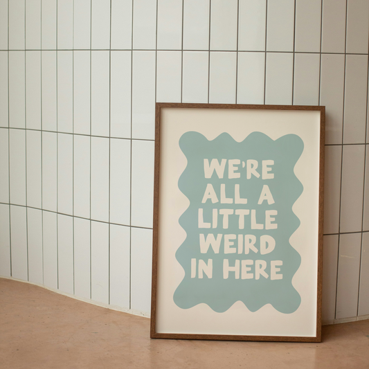 Framed poster with 'We're all a little weird in here' text on a tiled wall.